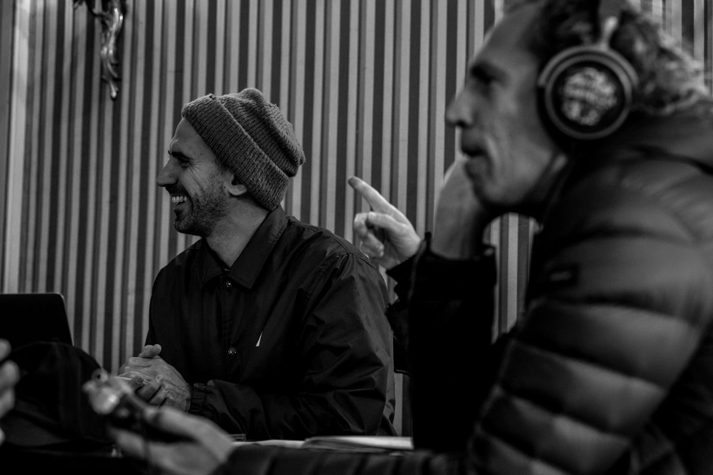 Stefano ride durante una registrazione, accanto a un uomo con le cuffie che alza il dito